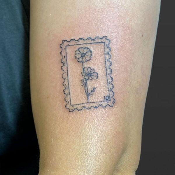 Atticus Tattoo| Fine line tattoo of a postage stamp with a stem of daises