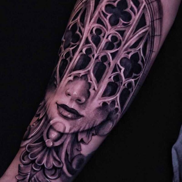 Atticus Tattoo| Black and grey realism tattoo of a gothic architecture window and woman's face