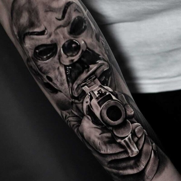 Atticus Tattoo| Black and grey realism tattoo of the Joker in a mask and pointing a gun