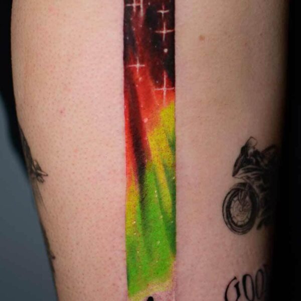 Atticus Tattoo| Colour realism tattoo of red and green Northern lights and the silhouette of a person.