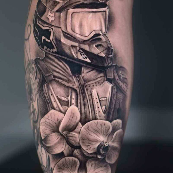 Atticus Tattoo| Realism tattoo of a dirt biker with a helmet on and orchids in front of them