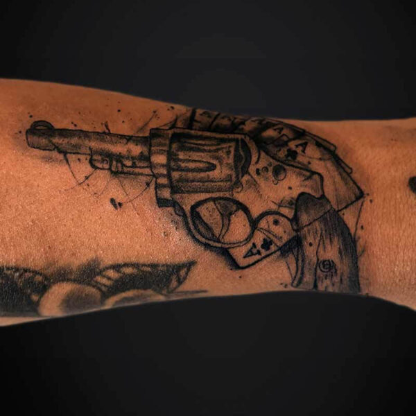Black and Grey Tattoo- Gun and Aces Atticus Tattoo| Black and grey tattoo of a pistol with ace cards and ink splashes