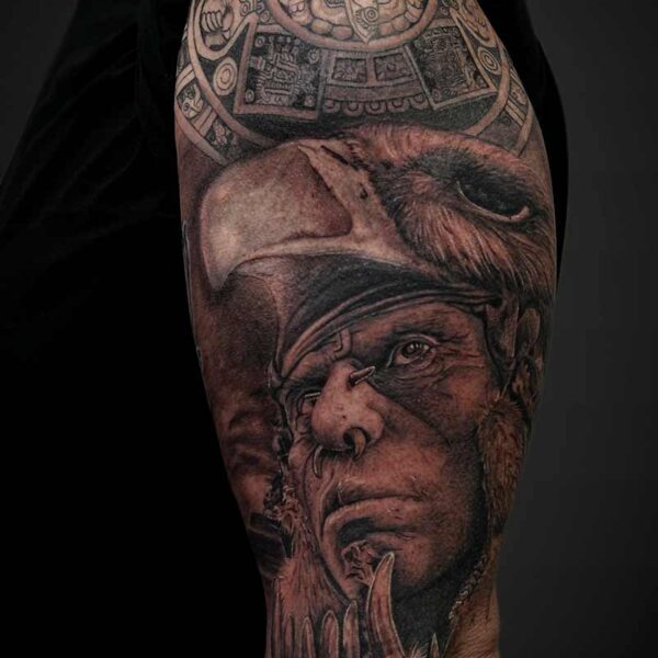 Black and Grey Realism Tattoo- Aztec Man and Calendar Atticus Tattoo| Black and grey realism tattoo of and Aztec man in a headdress with the Aztec stone calendar behind him