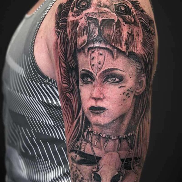 Black and Grey Realism Tattoo- Woman and Lion Atticus Tattoo| Black and grey realism tattoo of a woman with face tattoo, bone jewellery and wearing a lion skin