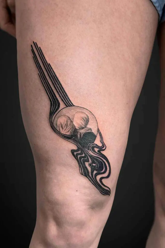 Black line-work tattoo of a stylized fork with three long tines and flowing decorative curves along a person's leg.