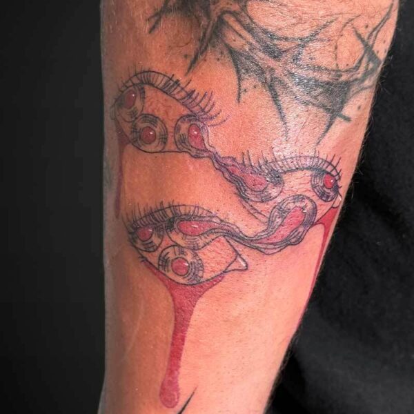 Forearm tattoo of a chain of round eyes connected by a sinewy line, red irises with a blood-like drip running down the forearm; dark thorny branches above.
