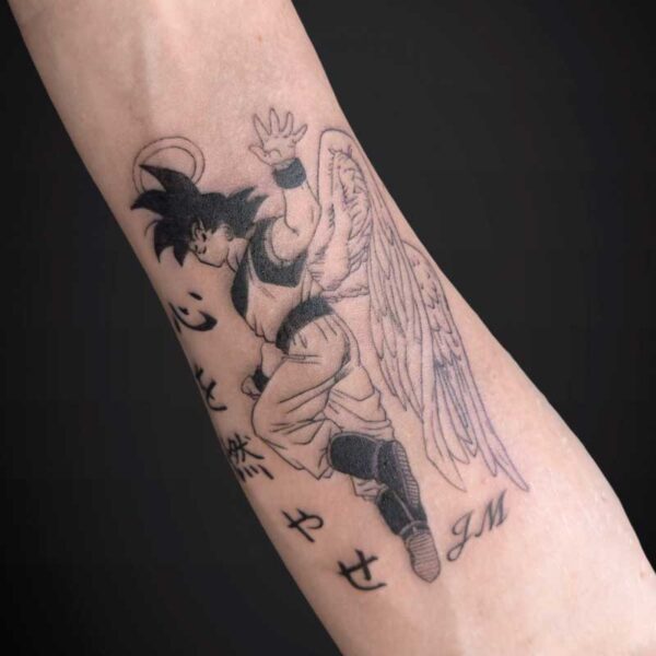 Forearm tattoo of Goku from Dragon Ball with large angel wings, black-and-gray linework and Asian characters along the arm.