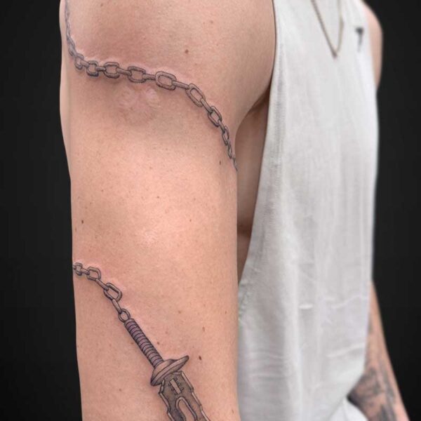 Arm tattoo featuring a chain wrapping from shoulder to mid-upper arm and a dagger tattoo on the forearm area.