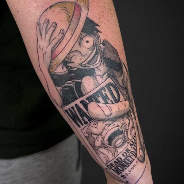 Tattoo of a cartoon pirate with a straw hat, covering one eye, holding a banner that says WANTED.