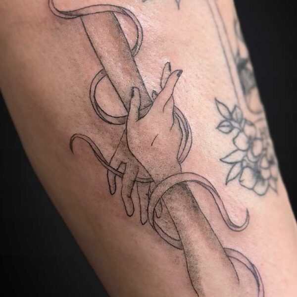 Hand gripping a curved, vine-wrapped staff in a black-and-gray tattoo with floral elements nearby