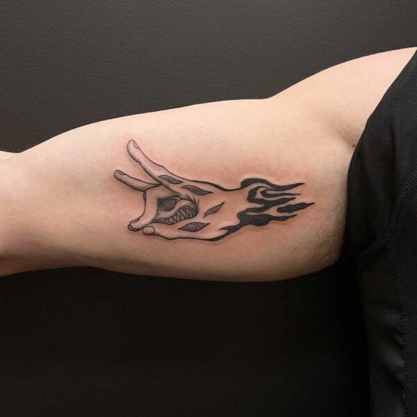 Tattoo on inner forearm: a stylized black flame with a gaping mouth and sharp teeth along the flame.