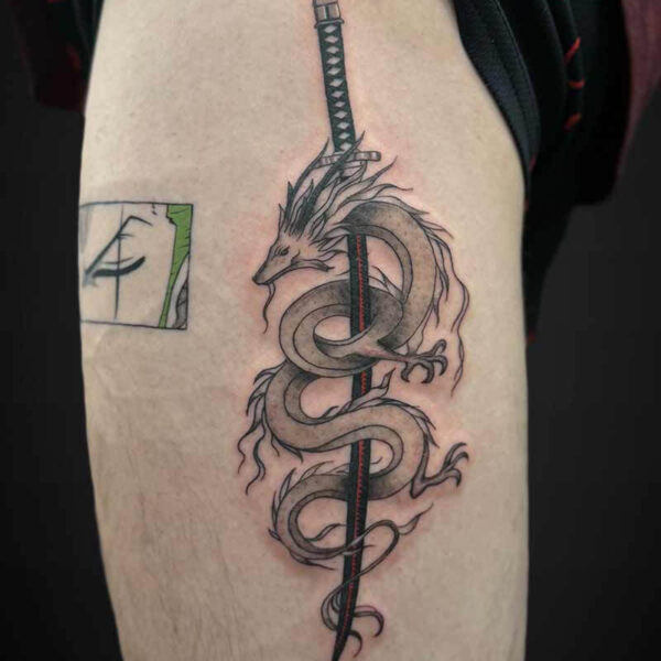Dragon coiled around a katana sword tattoo on the upper arm, with a black handle and red accents.