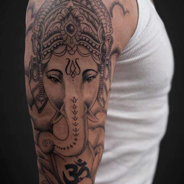 Tattoo of the Hindu deity Ganesha on a man's upper arm, featuring an ornate headdress and trunk.
