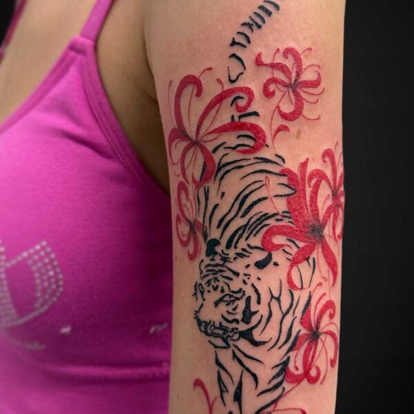 Tattoo on upper arm: black tiger outline with red tropical flowers and swirls, pink strap of the top visible.