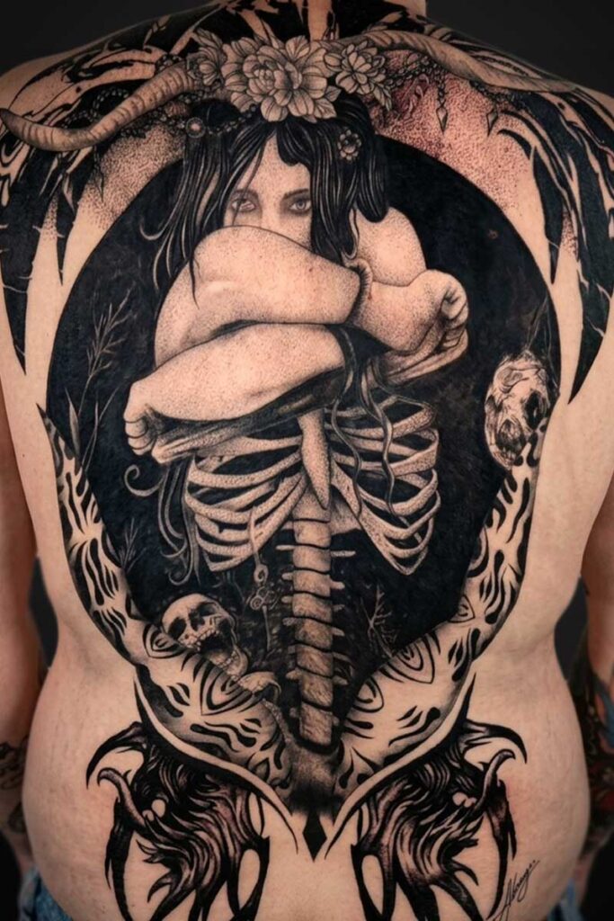 Back tattoo showing a curled woman inside a dark circular frame, with an exposed ribcage and skulls around the edges.