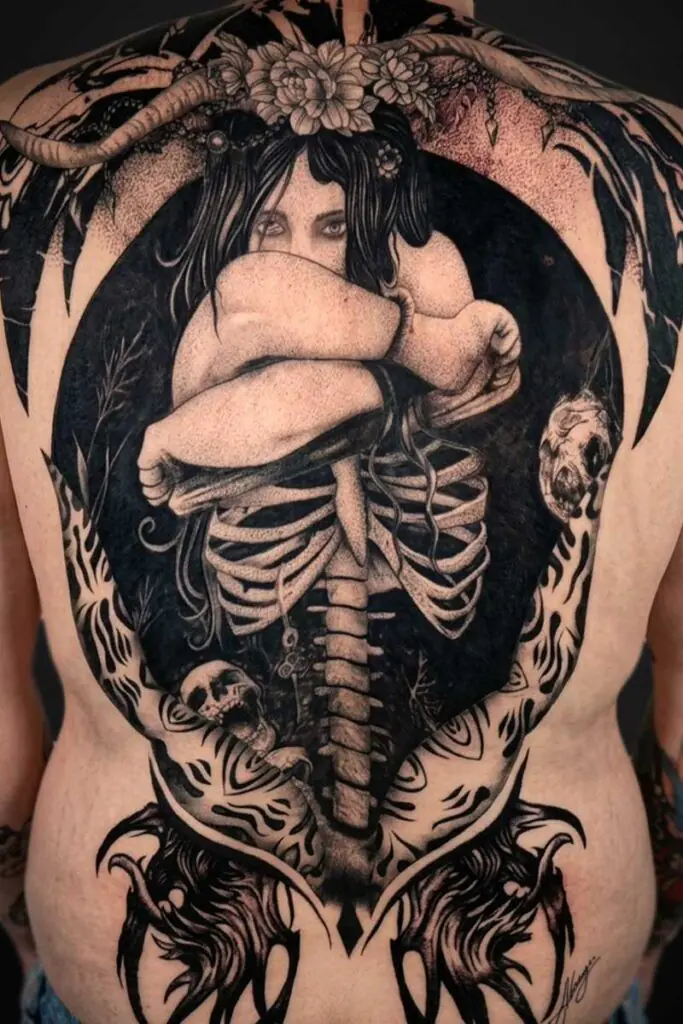 Back tattoo showing a curled woman inside a dark circular frame, with an exposed ribcage and skulls around the edges.