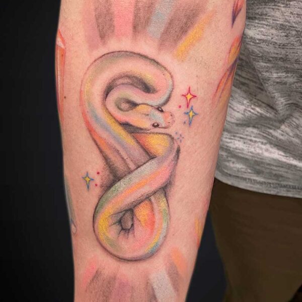 Colorful rainbow snake tattoo coiled along the forearm with pastel shading and small star accents.