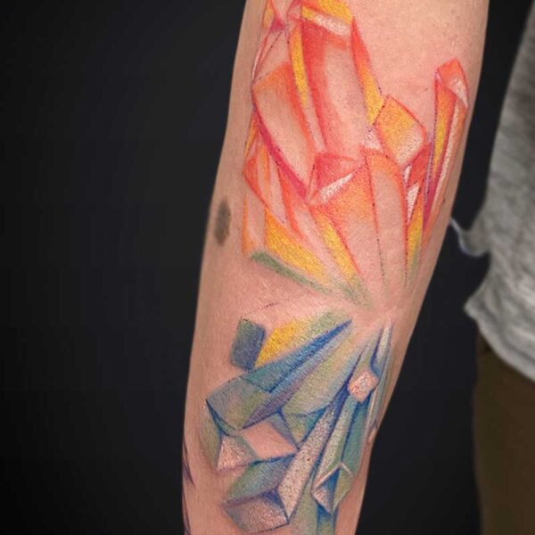 Forearm tattoo of abstract orange-red crystal shards above blue-green crystal shards.