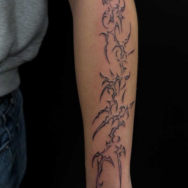 Black tribal-style vertical forearm tattoo with sword-like, jagged lines running from elbow to wrist.