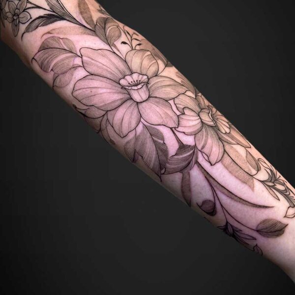 Forearm covered with a large black-line floral tattoo wrapping from wrist toward the elbow, featuring big petals and leaves on pale skin.