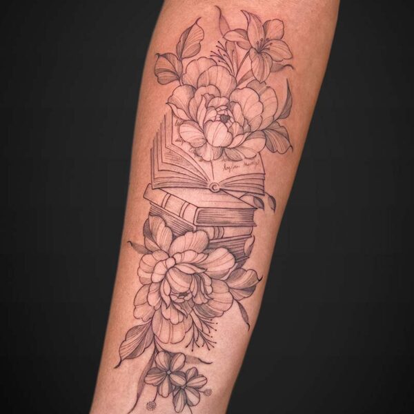 Forearm tattoo of an open book with large blooming flowers and leaves surrounding it.