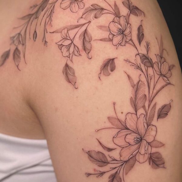 Delicate black-and-gray floral tattoo wrapping over the shoulder and upper arm with blossoms and leaves.