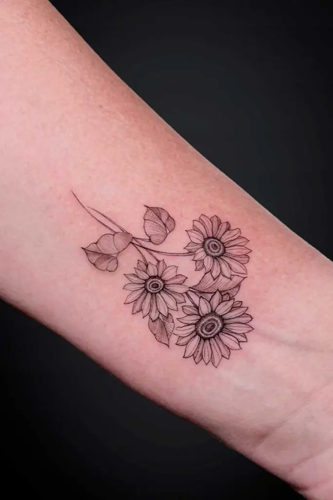 Line-drawn tattoo of three sunflowers with leaves on the inner ankle.