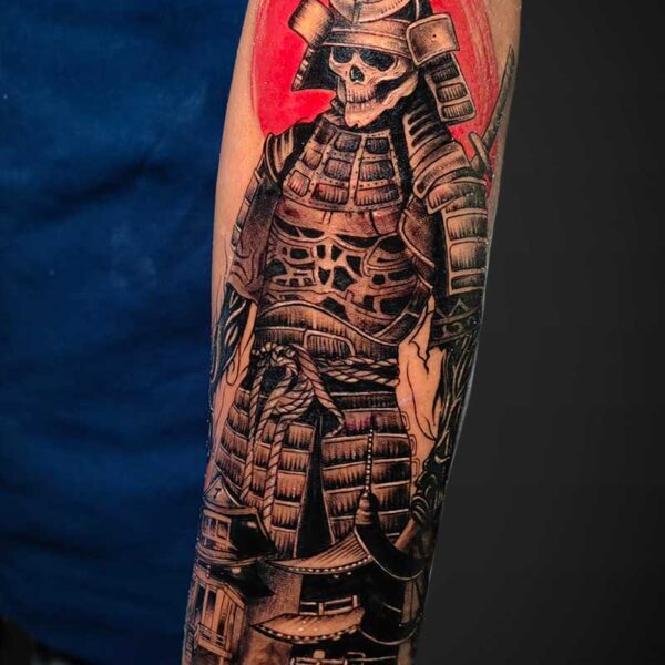 Forearm tattoo of a skull-faced samurai in traditional armor with a bold red circular backdrop behind the figure.