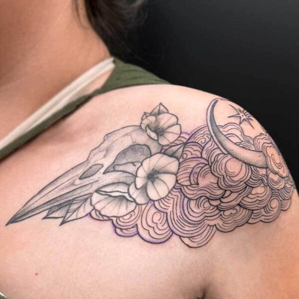 Shoulder tattoo featuring a bird skull with flowers and swirling cloud patterns