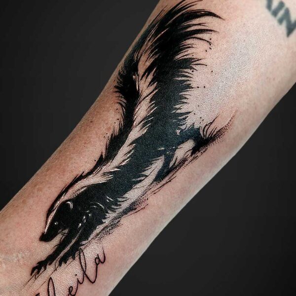Forearm tattoo of a stylized black creature with long, flowing spiky lines and cursive script reading 'Freedom' near the wrist.