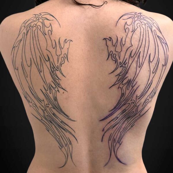 Back view of a person with large black wing outlines tattooed across the shoulder blades on an exposed back.