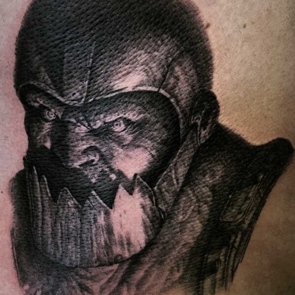 Close-up tattoo of a dark skull-like face with jagged teeth and a helmet on pale skin.