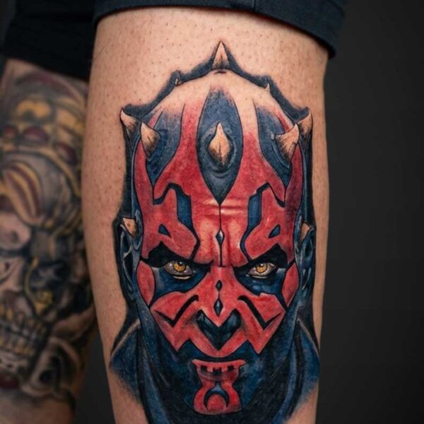 Colorful Darth Maul tattoo on the calf, red and black devilish mask with intense yellow eyes.