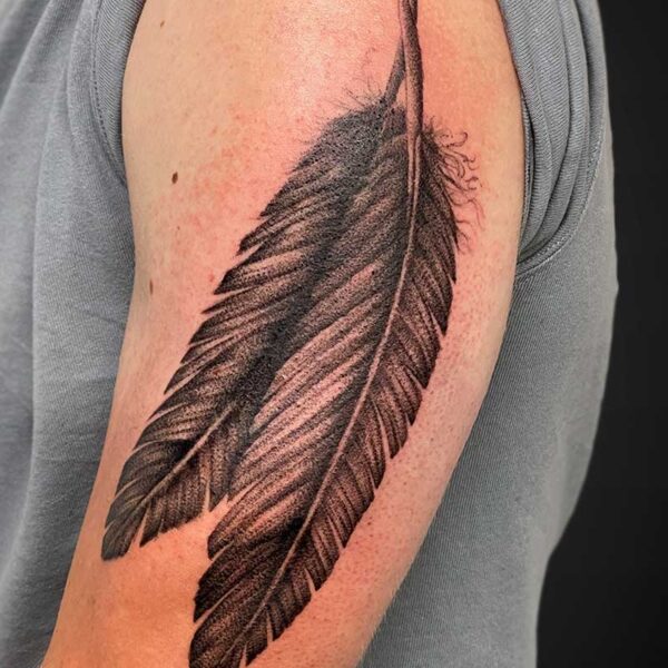Tattooed black feather running along the upper arm from elbow to shoulder area.