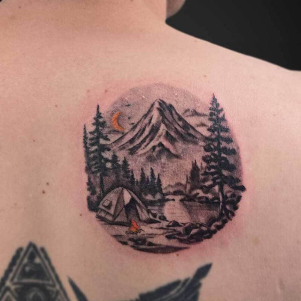 Circular back tattoo showing a mountain landscape with pine trees, a tent by a campfire, and a crescent moon in a forest scene.