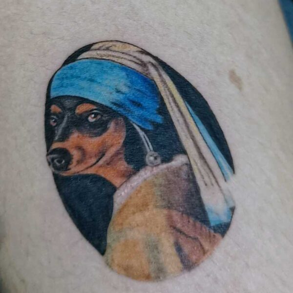 Oval tattoo of a Doberman wearing a blue nun's habit and veil.