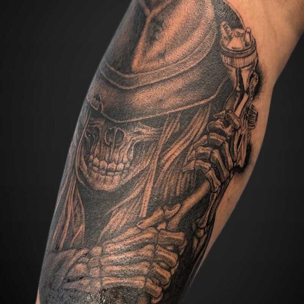 Grayscale tattoo of a Grim Reaper skeleton with a hood and scythe on a forearm, detailed shading and bone structure visible