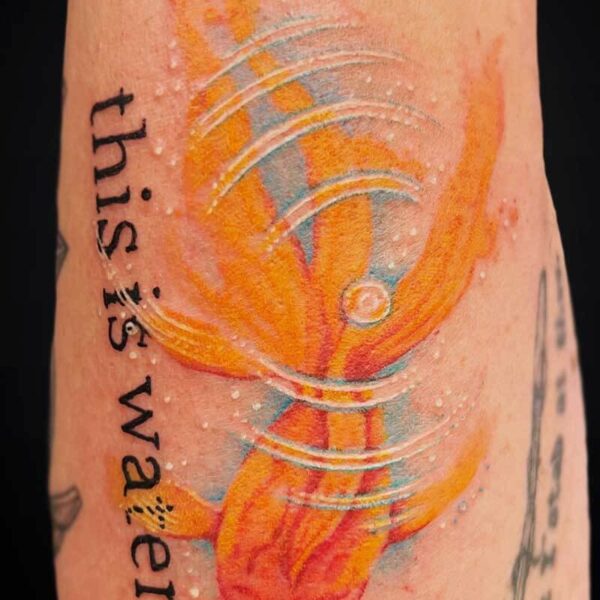 Colorful tattoo on an arm featuring orange and blue abstract shapes with white curved lines and vertical text along the side.