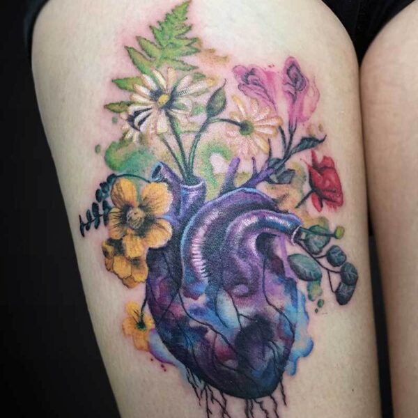 Colorful tattoo of a realistic heart with blooming flowers growing from it on the upper arm/forearm area, in watercolor style.