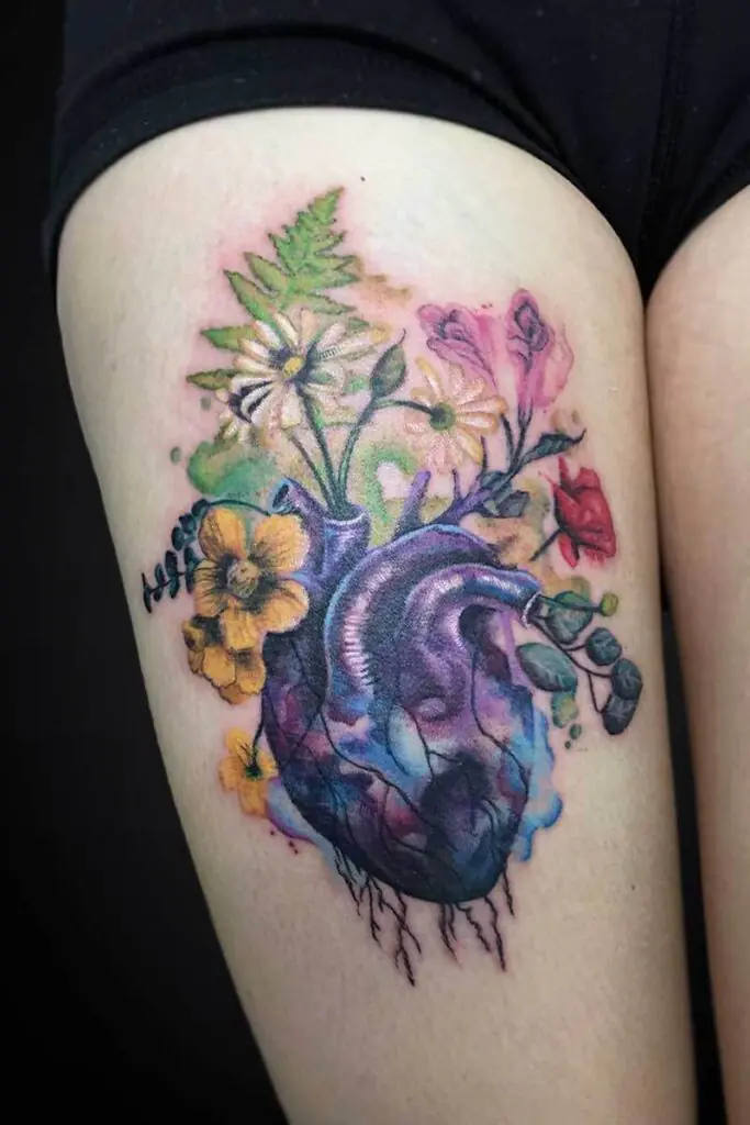 Colorful tattoo of a realistic heart with blooming flowers growing from it on the upper arm/forearm area, in watercolor style.