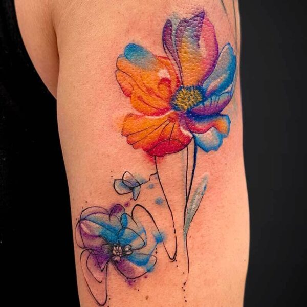 Watercolor-style tattoo of two colorful flowers on the upper arm, with orange/pink and blue/purple petals and delicate black line stems.