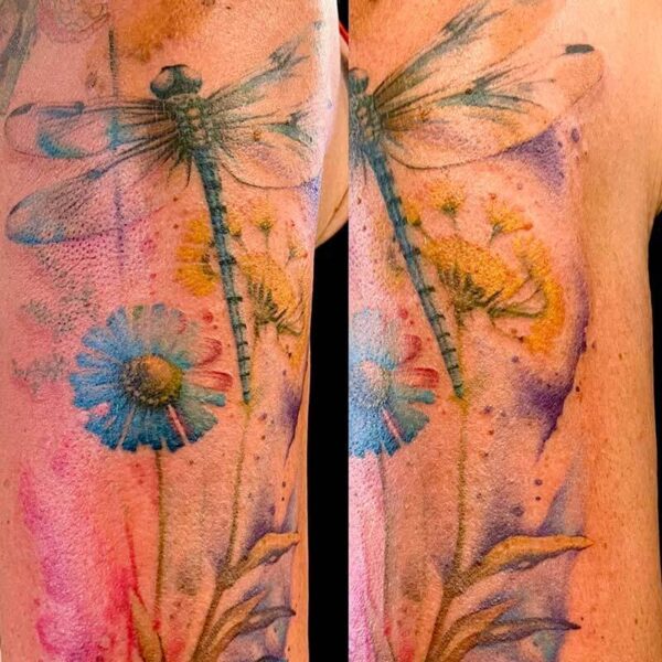 Watercolor-style dragonfly tattoo with blue daisies on the upper arm, pink, purple, and yellow background.
