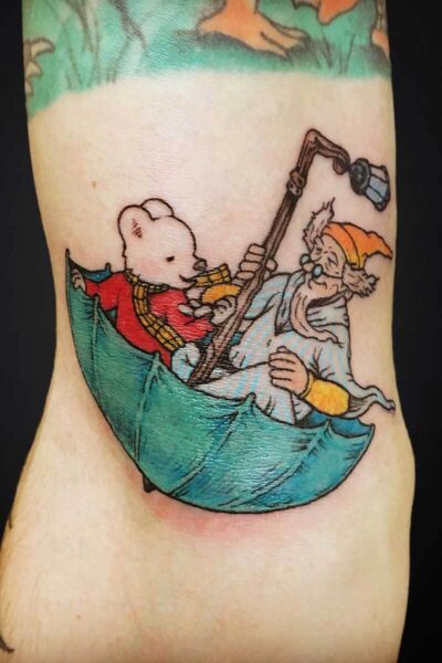 Cartoon tattoo on the leg showing Winnie the Pooh and an old bearded man in a small green boat at sea.