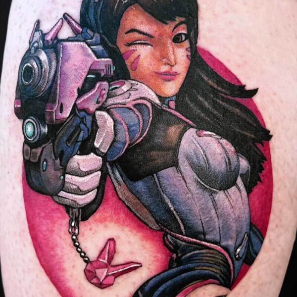 Colorful tattoo of a female character in futuristic armor, pointing a large gun toward the viewer with a wink, pink background.
