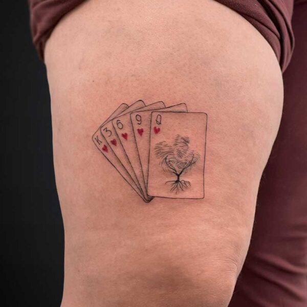 fineline-tattoo-cards-hearts Tattoo on the thigh: five playing cards fanned out with a tree-and-root design on the rightmost card, hearts on some cards
