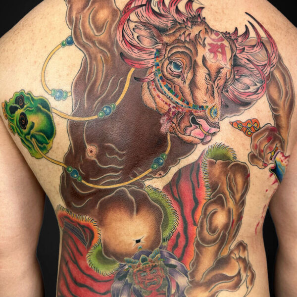 Full-back tattoo featuring a muscular brown bull with prominent horns, a red mane, and decorative turquoise-bead necklaces, set against swirling colorful patterns on the back.