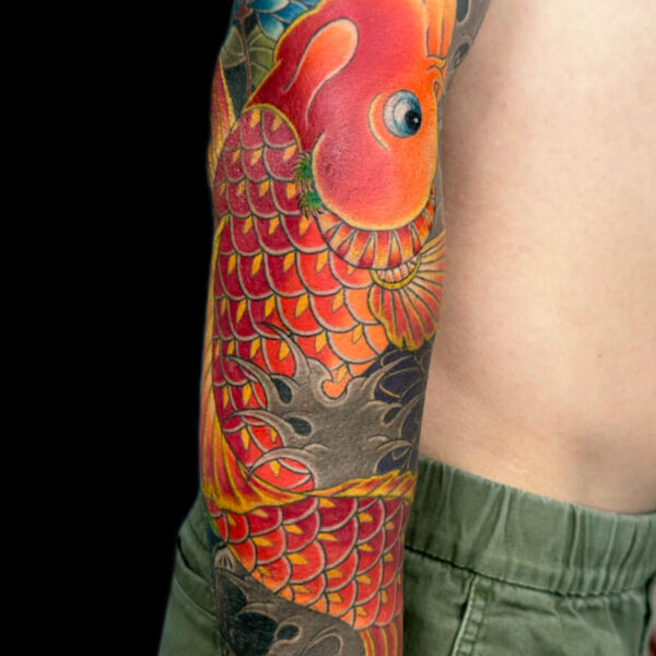 Colorful koi fish tattoo wrapping around the forearm with orange and red scales and blue accents against a dark background.