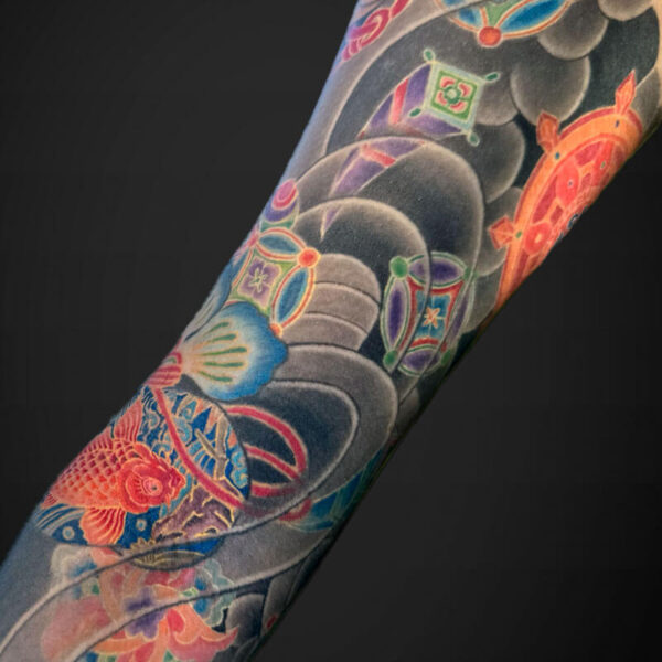 Close-up of a colorful full-sleeve tattoo on an arm, with koi fish, flowers and decorative motifs.
