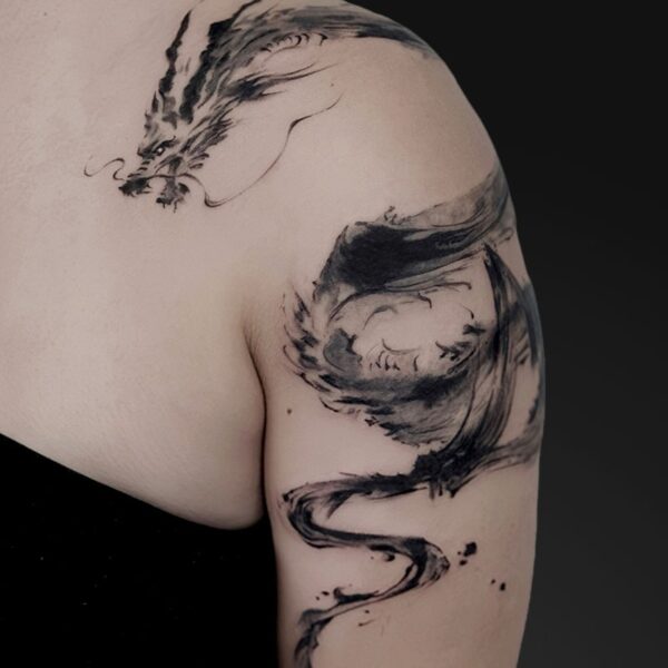 Abstract black ink dragon tattoo curling along the shoulder and upper arm in brushstroke style.