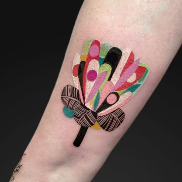 Colorful abstract flower tattoo on forearm with a brown striped bow around the stem.
